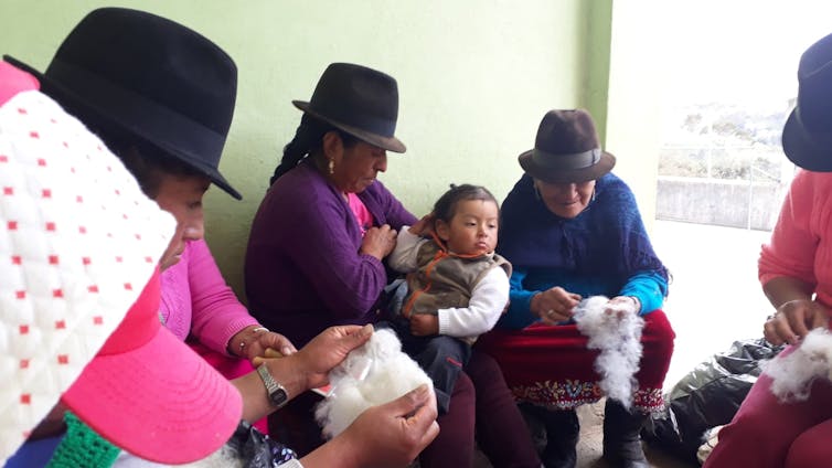 A group of women weave, a child sits on one of the women's laps.