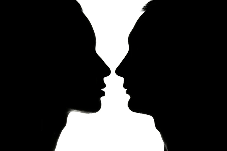 Siluetas enfrentadas de perfil de hombre y mujer en negro sobre blanco.