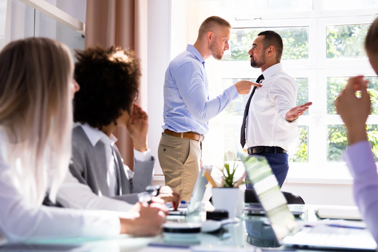 Stressed businesspeople sitting In front of a colleague bullying another.