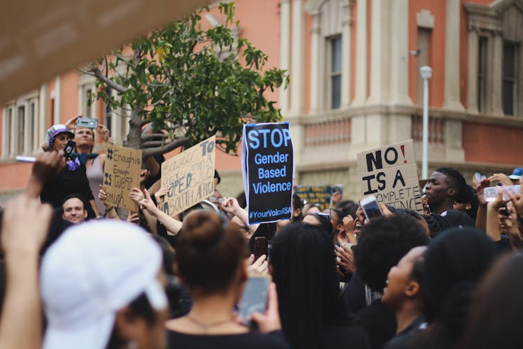 A crowd of protestors hold up signs in a street setting.