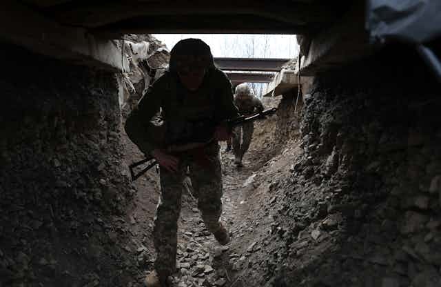 A Ukrainian fighter in fatigues and holding a gun enters a tunnel.