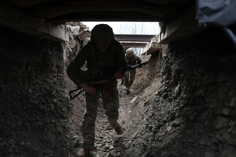 A Ukrainian fighter in fatigues and holding a gun enters a tunnel.