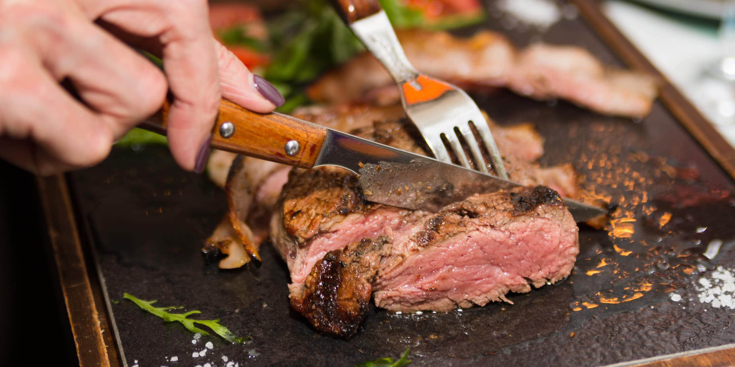 Une personne coupe un morceau de viande rouge
