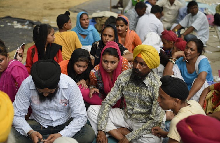 Sikh men wearing colorful turbans and women with their heads covered gather together.