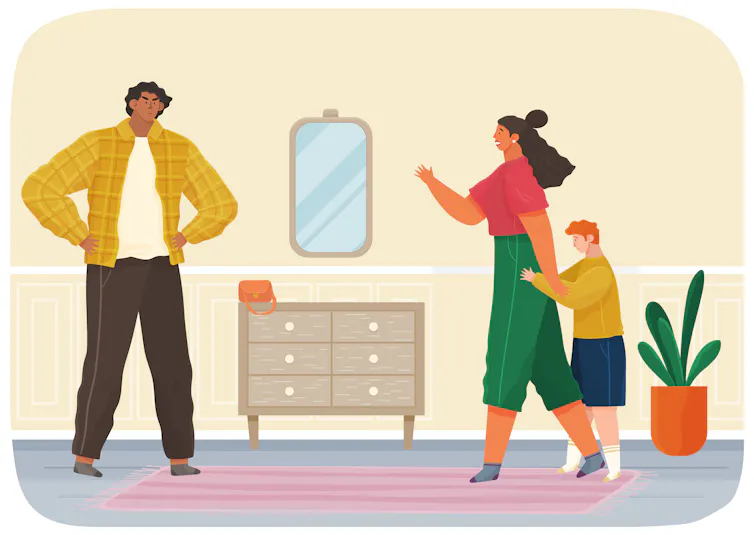 One parent stands alone on one side of a room, while another parent stands in front of a child