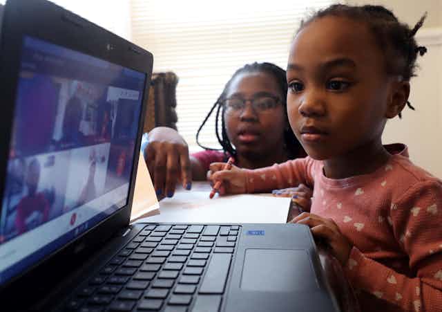 woman helps young girl on Zoom on laptop