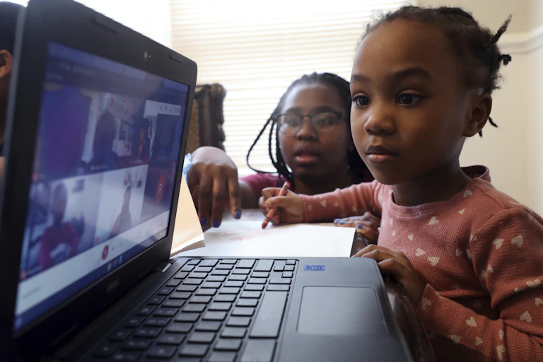 woman helps young girl on Zoom on laptop
