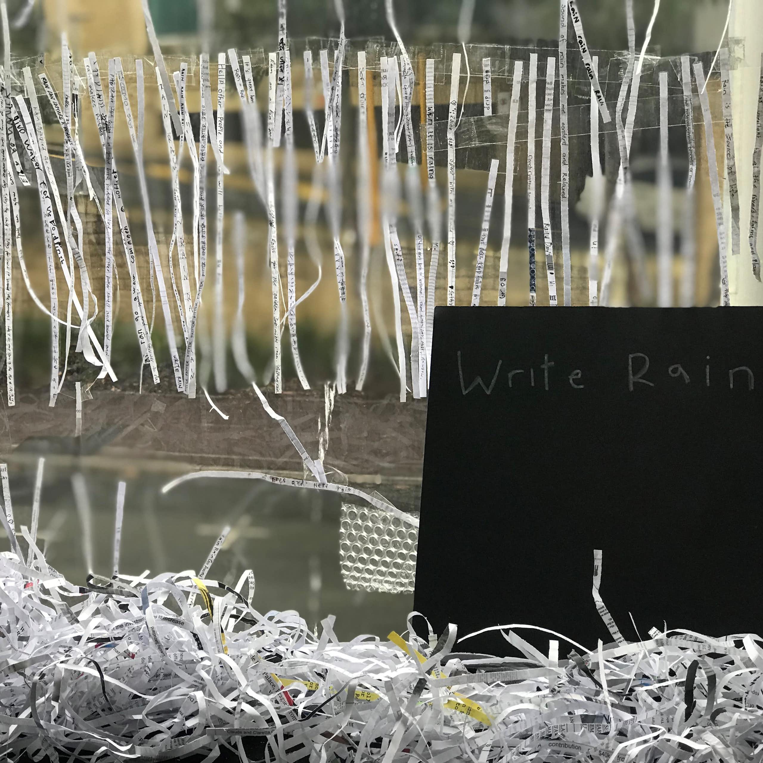 A chalkboard saying 'write rain' is seen alongside many very thin strips of paper with writing on them.