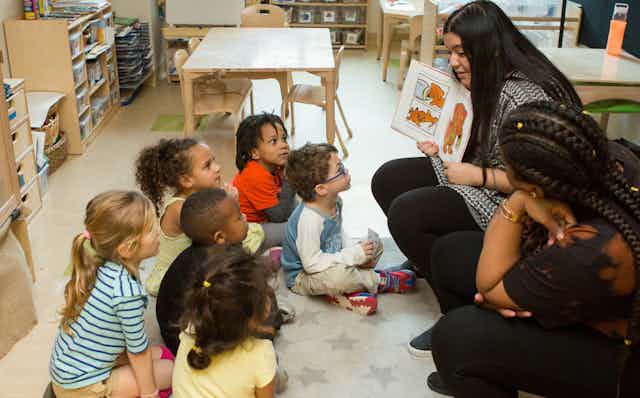 Two early childhood educators seen reading a book to a circle of children.