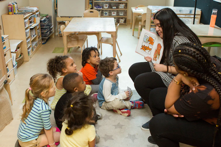 Two early childhood educators seen reading a book to a circle of children.