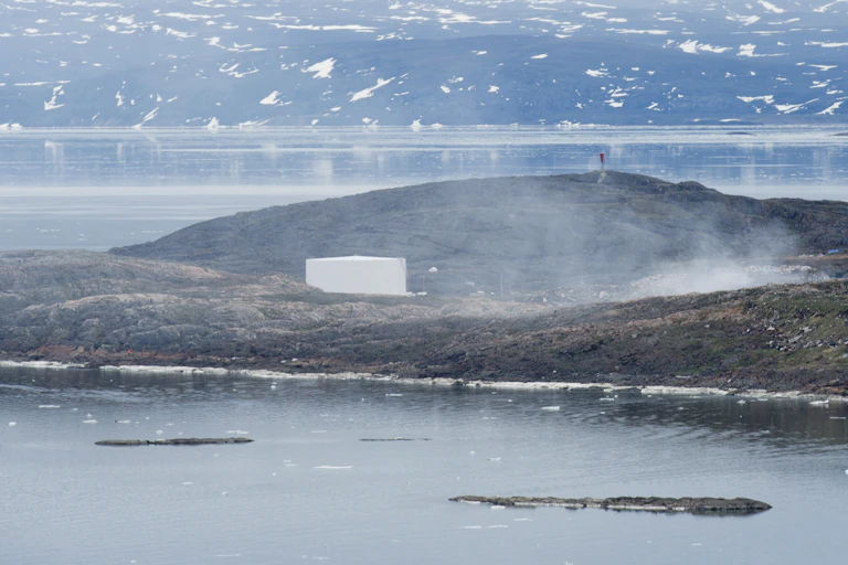 The garbage dump fire is seen smoldering across a bay with mountains in the background