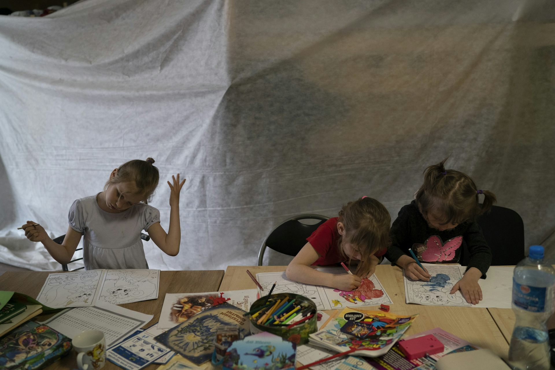 Attablés sous une tente, des enfants dessinent