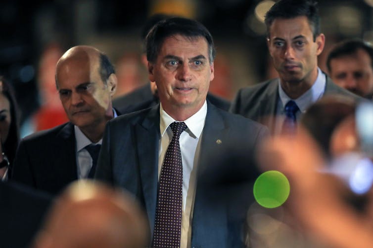 Bolsonaro walks toward cameras with men behind him.