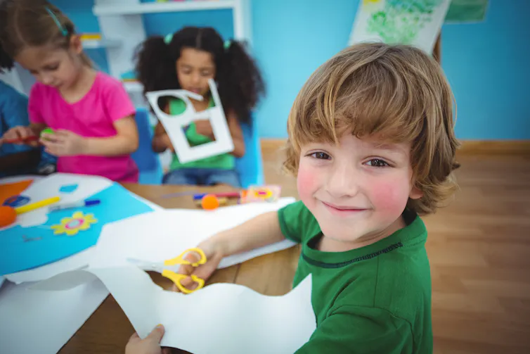 Des enfants souriants font du découpage à la maternelle