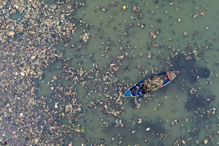 Aerial shot of boat floating through plastic pollution on water
