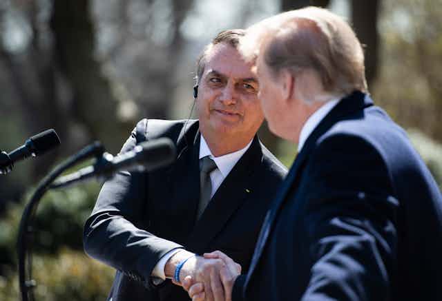 Bolsonaro smiles as he shakes Trump's hand at an outdoor news conference on a sunny spring day.