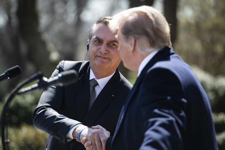 Bolsonaro smiles as he shakes Trump's hand at an outdoor news conference on a sunny spring day.