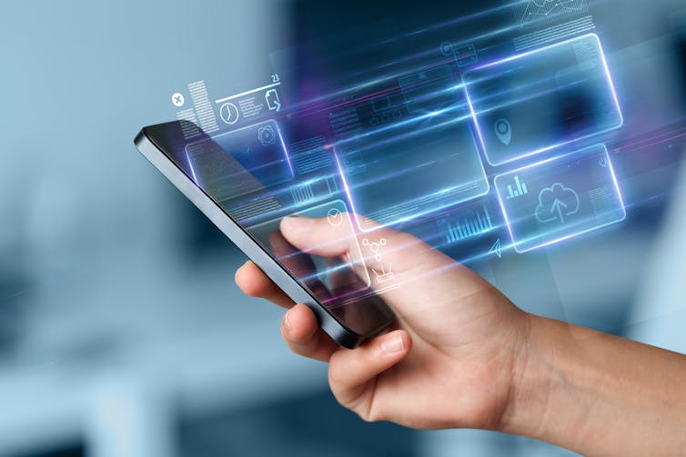 a hand holding a smart phone with blurred purple icons floating above it