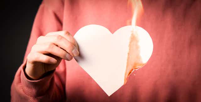 Una persona con un corazón de papel ardiendo sobre jersey rojo.