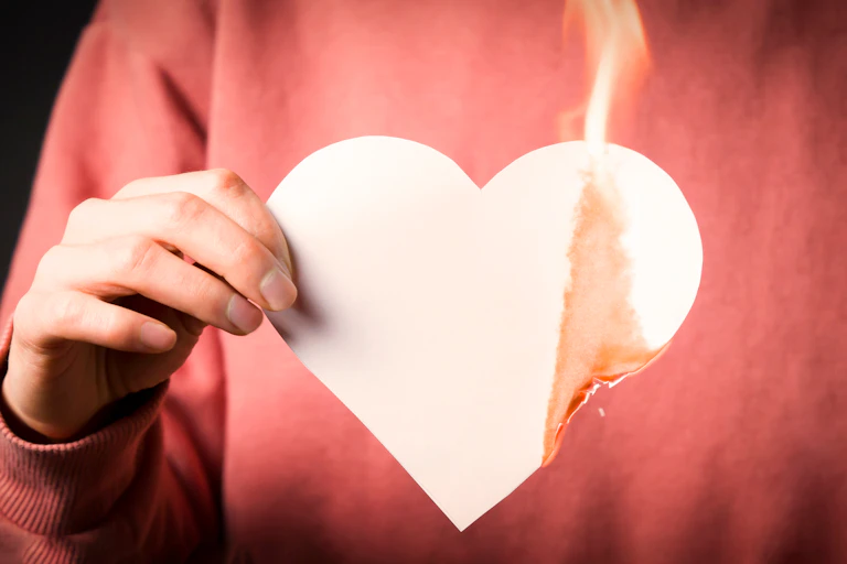 Una persona con un corazón de papel ardiendo sobre jersey rojo.