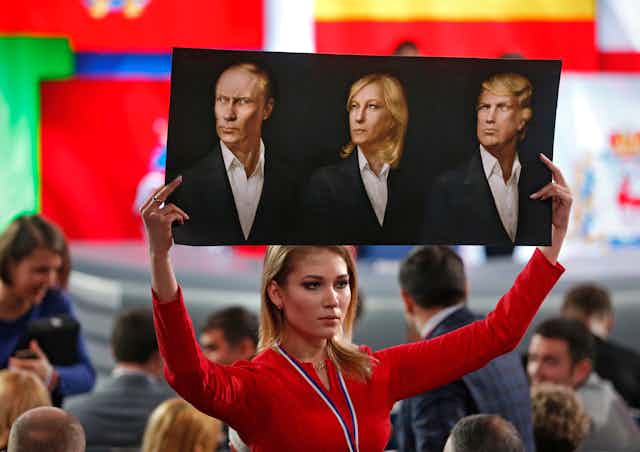 A woman holds up a poster showing Vladimir Putin, Marine Le Pen and Donald Trump.