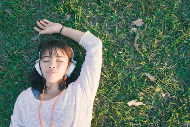 Wanita berbaring di rumput memakai headphone