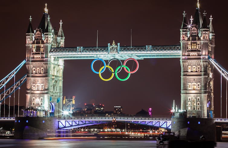 Tower Bridge in London at night with olympic rings hanging from it.