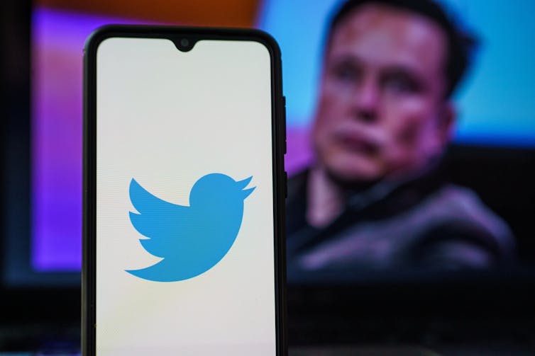 Smartphone showing Twitter logo with Elon Musk in the background