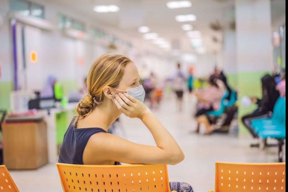 A woman in a surgical mask sits in a hospital waiting room.