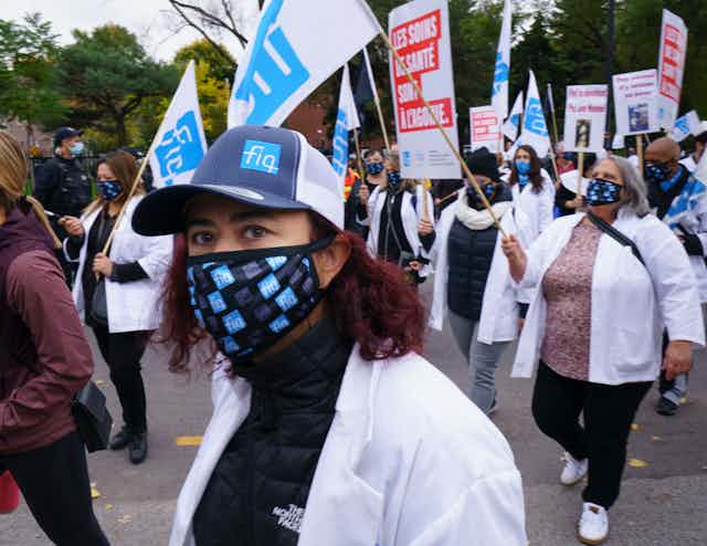 A woman in a face mask and hat in the foreground with marching protesters in the background