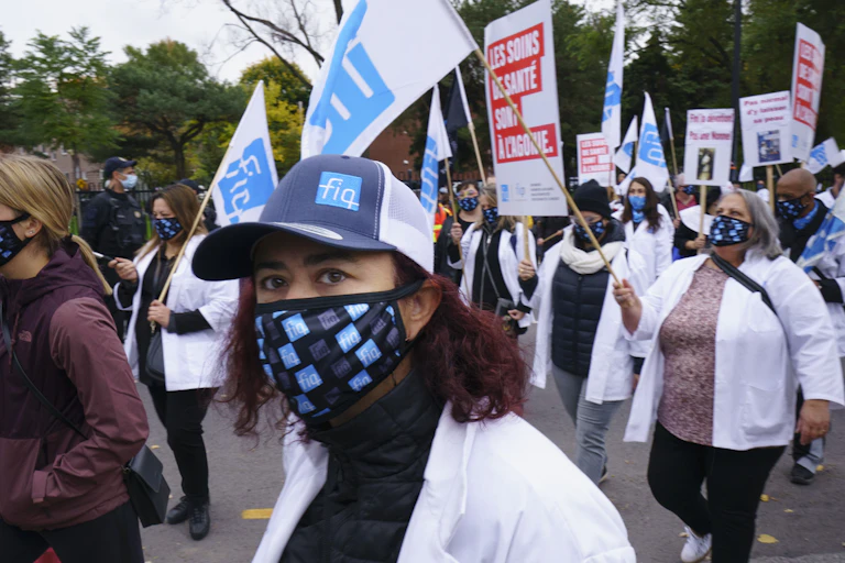 A woman in a face mask and hat in the foreground with marching protesters in the background