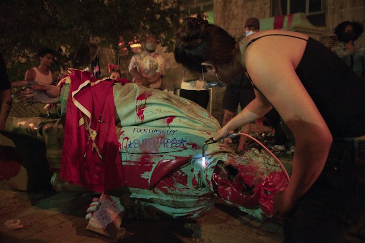 A woman takes a torch to the head of a statue