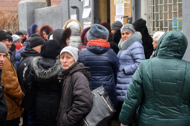 People dressed in winter coats looking worried and waiting for something outside a building.