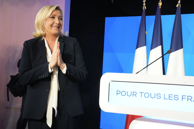Marine Le Pen, les mains jointes, à côté de drapeaux français.