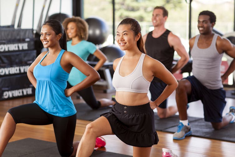 A group of people in workout clothes in a gym doing lunges.