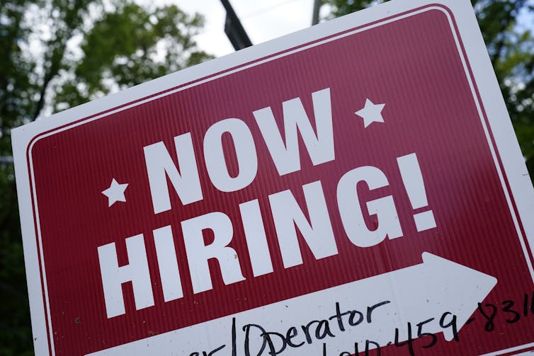 a red sign with white letters reads 'now hiring!'