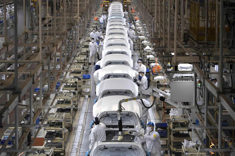 A photo showing a production line full of partly-assembled cars and several workers.