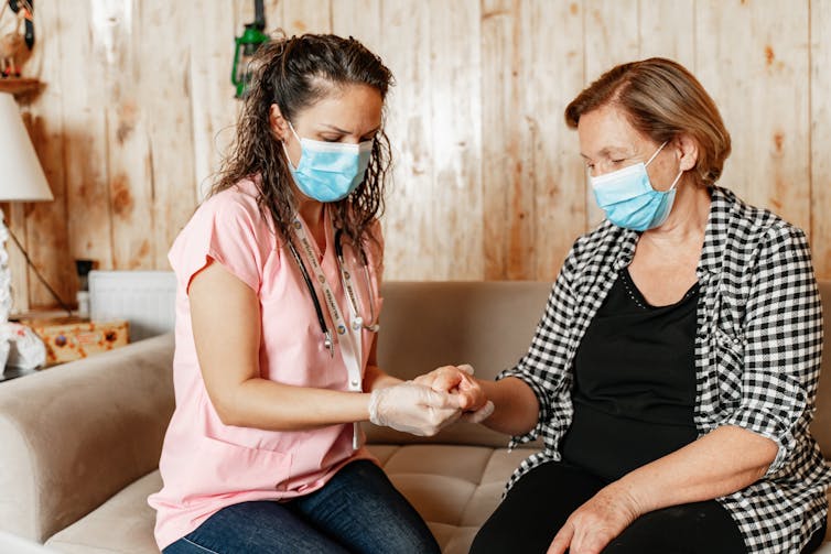 Woman in mask holds hand of an older woman.