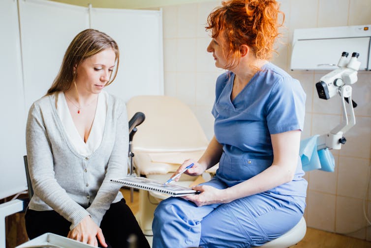 Doctor in scrubs shows patient a form.