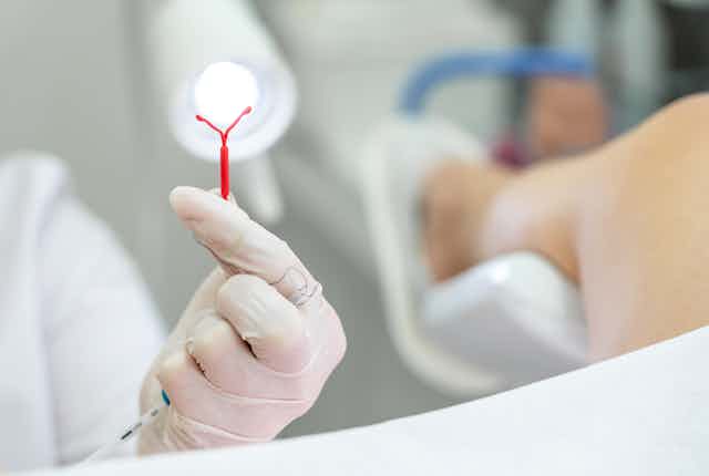 A gloved hand holding up a red plastic IUD