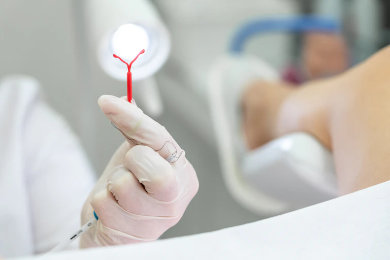 A gloved hand holding up a red plastic IUD