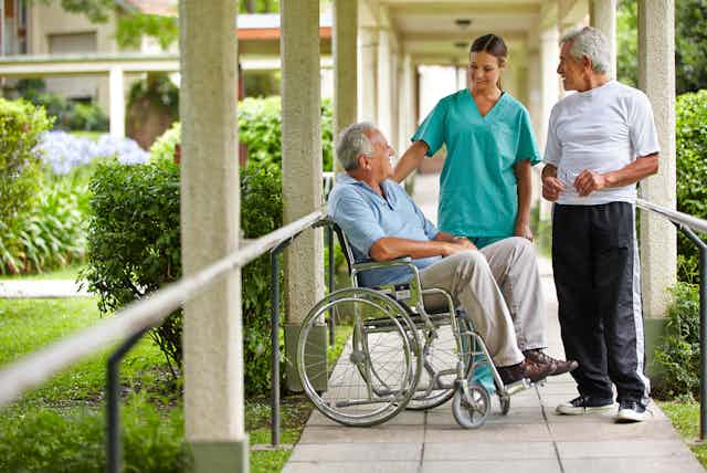 Elderly wheelchair user talking to care staff outside on ramp