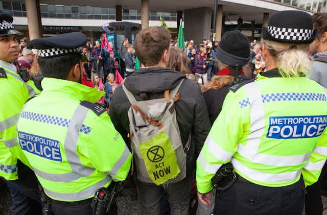Rear view of an extinction rebellion protest, with one protester standing between two police officers