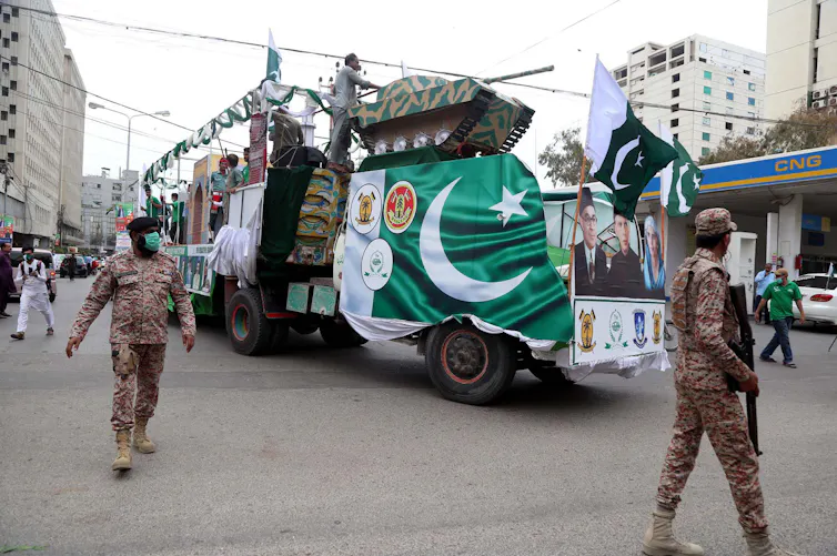 Two men wearing military-style uniforms and carrying guns police a parade in Karachi