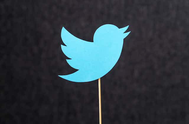 A cardboard cut-out of the Twitter logo on a stick against a black background.