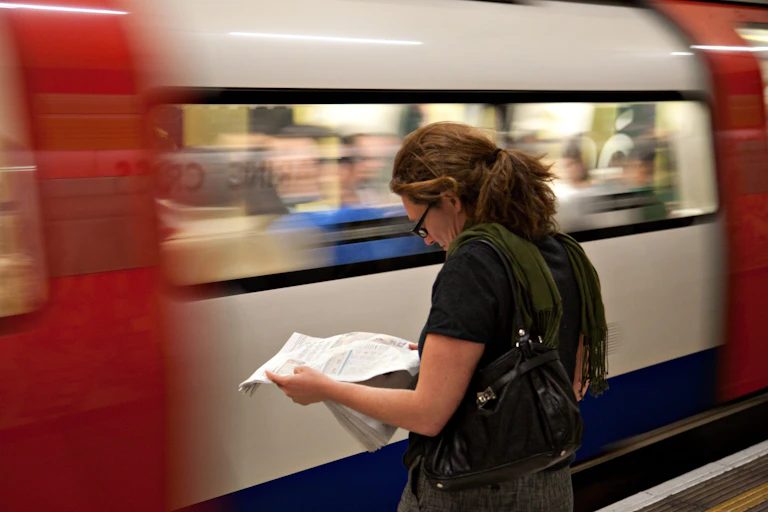 A woman reads a newspaper as a blurred Tube train passes at speed