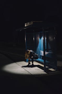 A woman sits alone at night at a bus stop