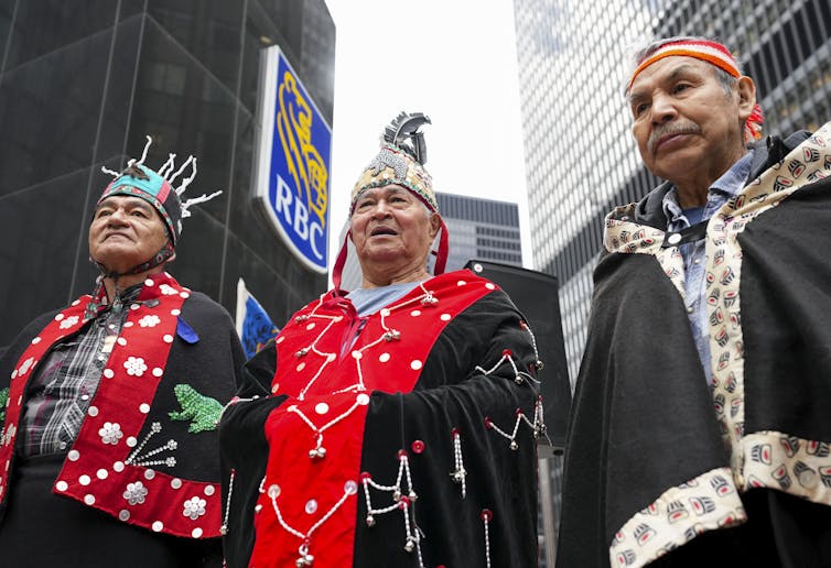 Three men stand in front of tall office buildings, one with the sign RBC