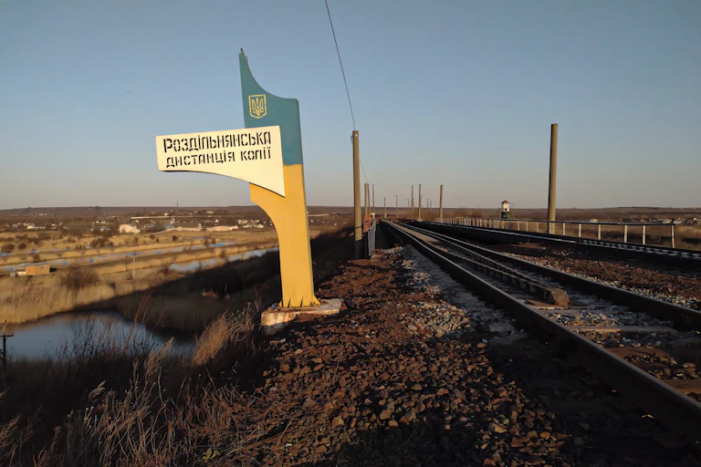 A large Soviet looking sign stands next to an empty railroad track
