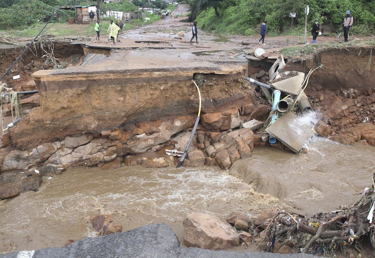 People stand along a road, where a bridge once stood.